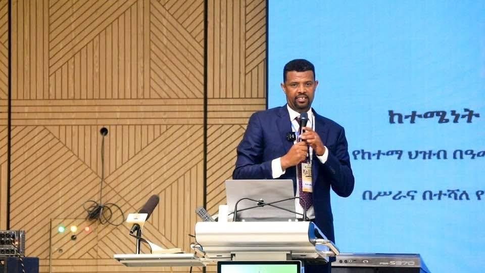A speaker teaching from a lectern with a screen behind him.