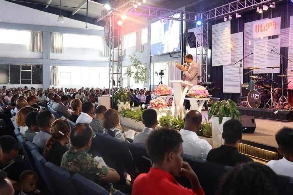 A speaker addressing a congregation in a large hall.