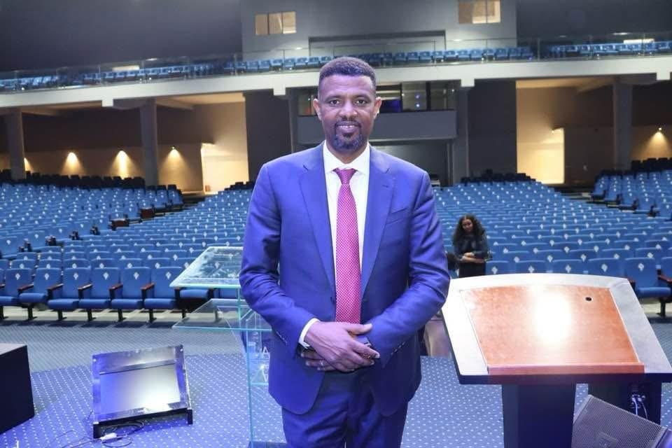 A ministry participant standing near a lectern in an auditorium.